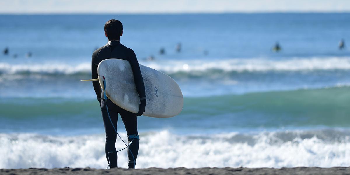 サーフボードを持ち海を見つめているサーファーの写真